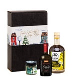 Eine Flasche Rapsöl und ein Glas Kräuterbutter-Gewürzmischung der Marke Die Ölfreunde und eine Flasche Apfelessig der Marke Die Essig Brauerei, vor einer Weihnachts-Geschenkeverpackung.