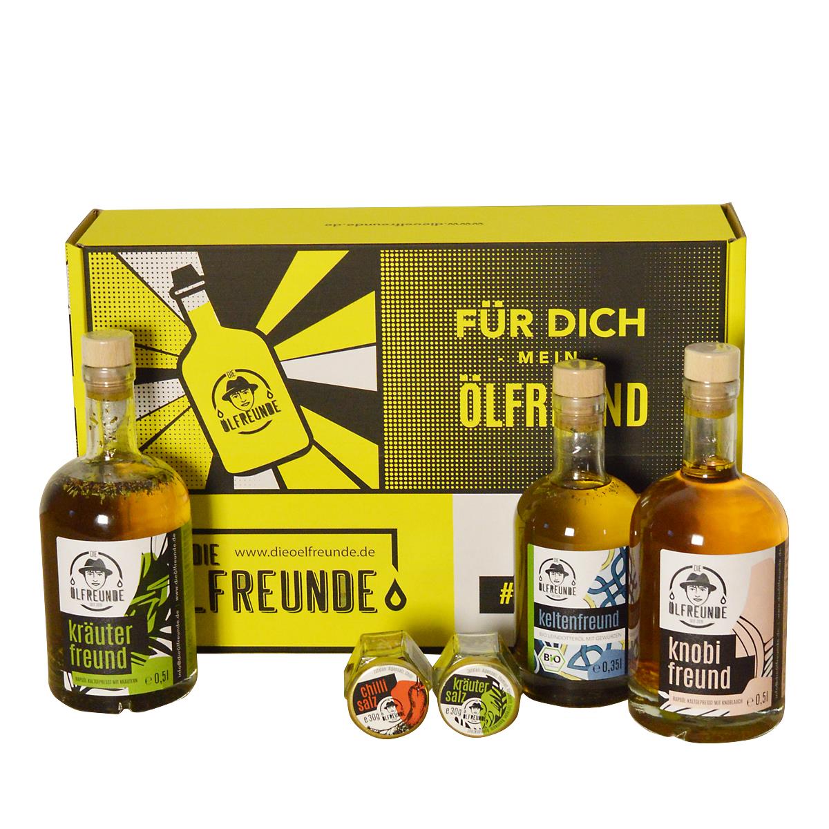 Eine Flasche Kräuteröl, Knoblauchöl, Leindotteröl mit Gewürzen, Chillisalz und Kräutersalz, der Marke Die Ölfreunde, vor einer gelben Geschenkeverpackung.