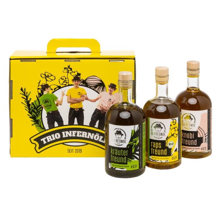 Ein Set mit einer Flasche Kräuteröl, Rapsöl und Knoblauchöl der Marke Die Ölfreunde, vor einer gelben Geschenkeverpackung.