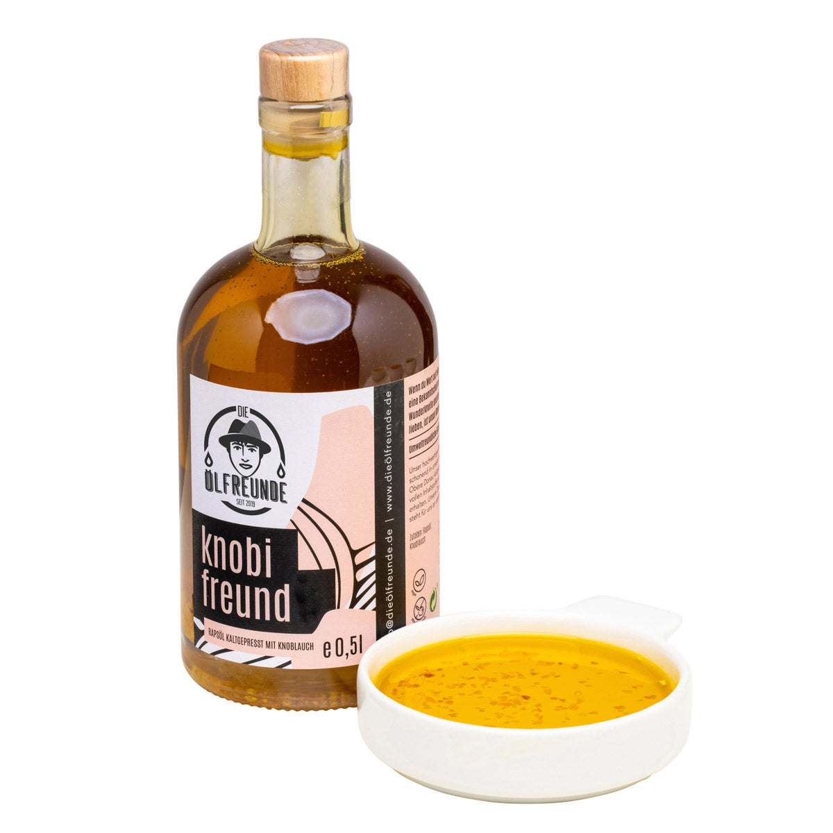 Eine Flasche mit 500ml kaltgepresstes Knoblauchöl mit Knoblauchstücken von Marke Die Ölfreunde, daneben eine Schale mit Knoblauchöl.