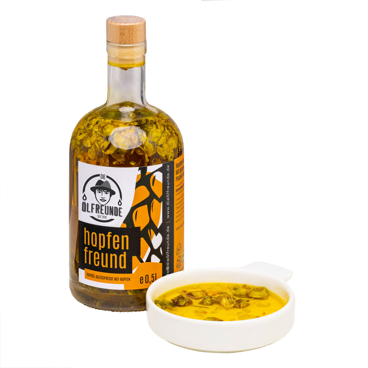 Eine Flasche mit 500ml kaltgepresstes Rapsöl mit Hopfen, der Marke Die Ölfreunde, daneben eine Schale mit Hopfen-Öl.