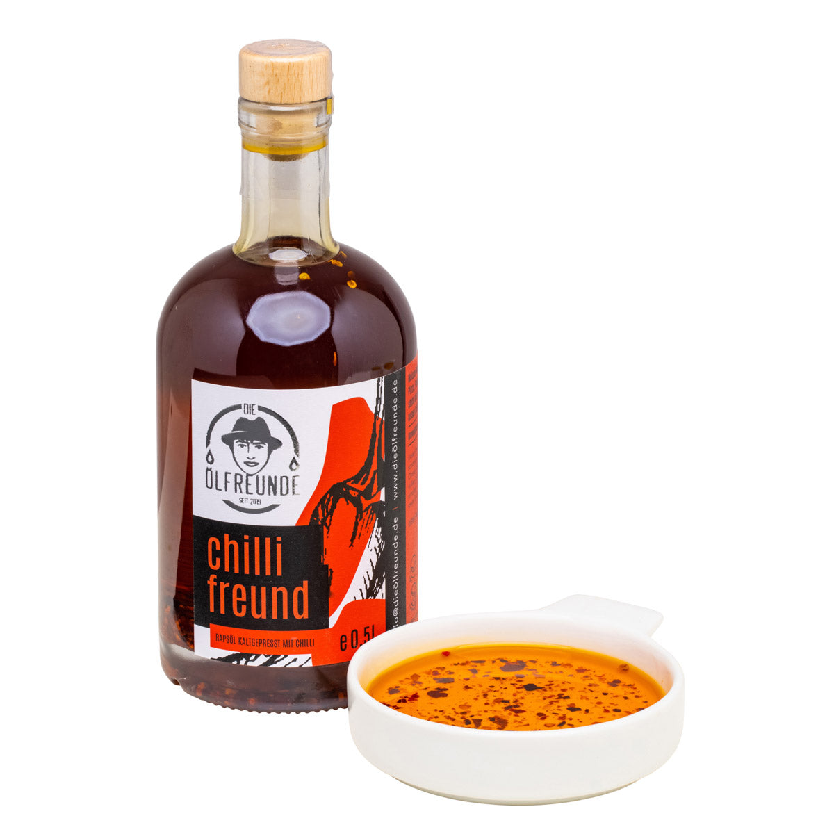 Eine Flasche mit 500ml kaltgepresstes crispy Chilli-Öl mit Chilliflocken, von Marke Die Ölfreunde, daneben eine Schale mit Chilliöl.