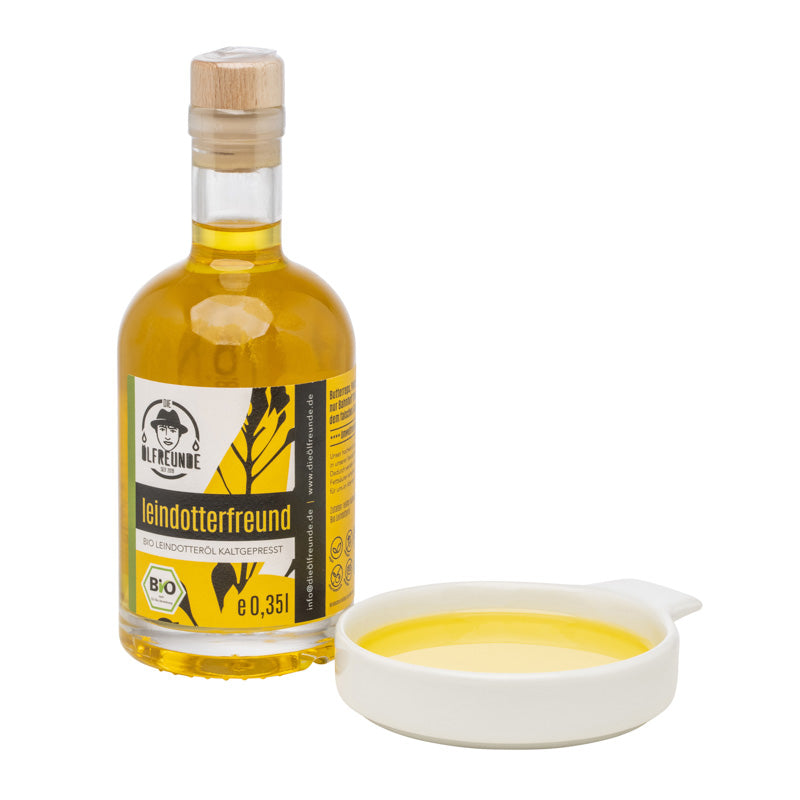 Eine Flasche mit 350ml Bio-Leindotteröl der Marke Die Ölfreunde, daneben eine Schale mit Leindotteröl.