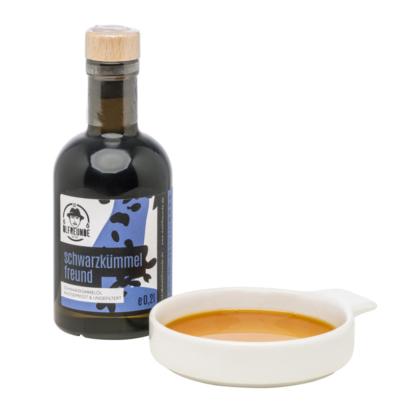 200ml Flasche Schwarzkümmelöl der Marke Die Ölfreunde, daneben eine Schale mit Schwarzkümmelöl.
