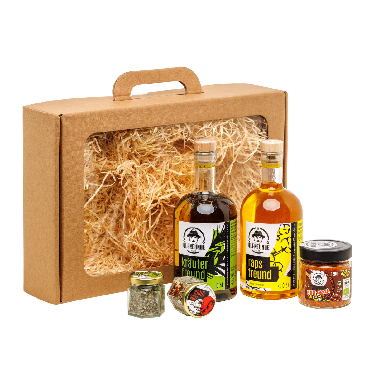 Eine Flasche Kräuteröl, Rapsöl, ein Glas Kräutersalz, Chillisalz und BBQ-Gewürzmischung, der Marke Die Ölfreunde, vor einer Geschenkeverpackung.