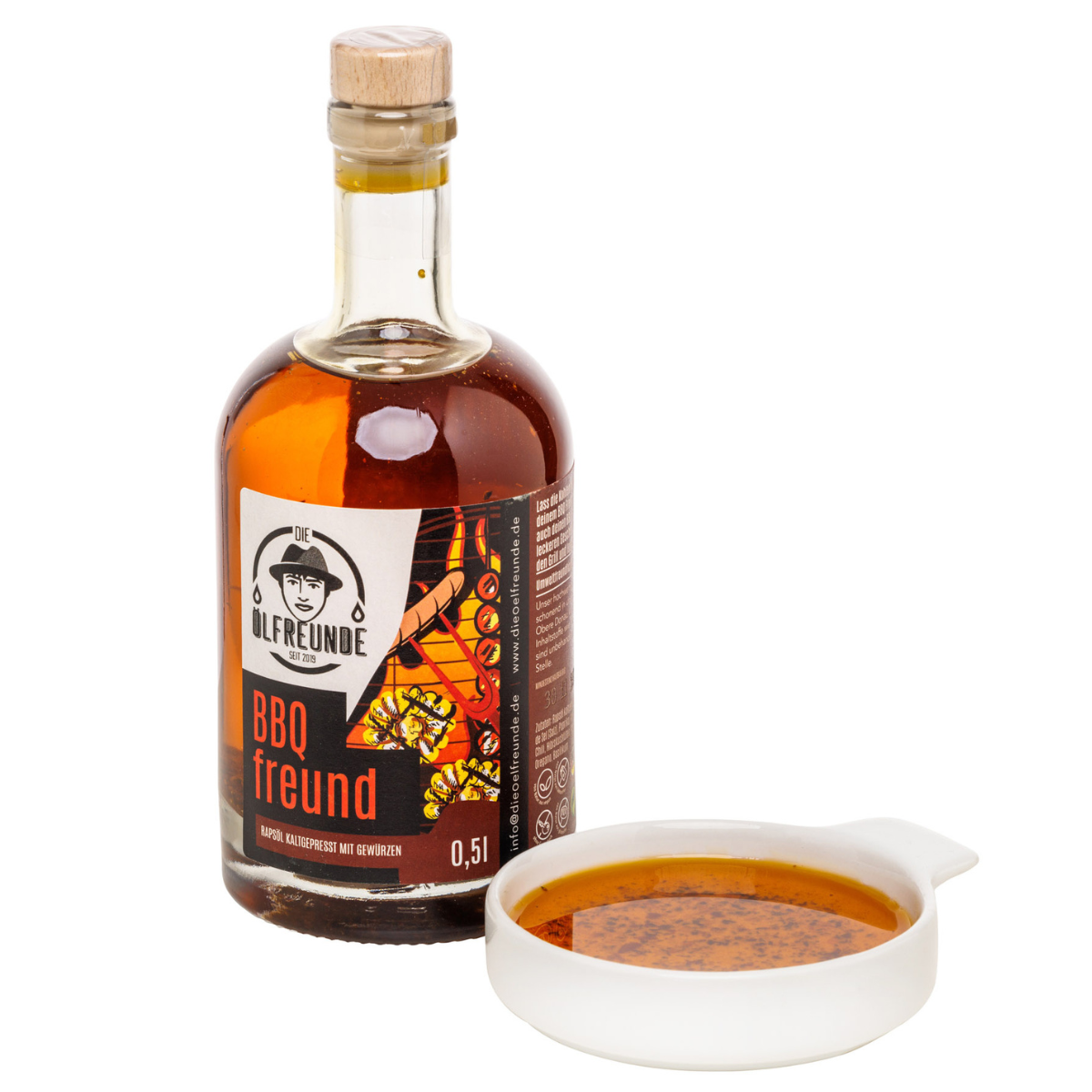 500-ml-Flasche kaltgepresstes Rapsöl mit BBQ-Gewürzen wie Paprika, Chilli, Hibiskusblüten, Knoblauch, Basilikum, von Marke Die Ölfreunde, daneben eine Schale mit BBQ-Öl.