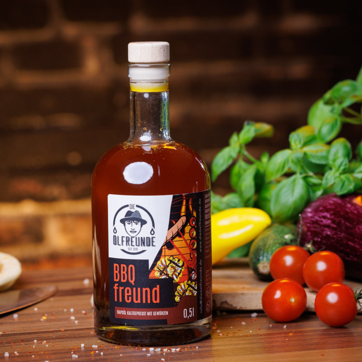 Eine 500-ml-Flasche BBQ-Öl der Marke Die Ölfreunde, auf rustikalem Holztisch, daneben frisches Gemüse.