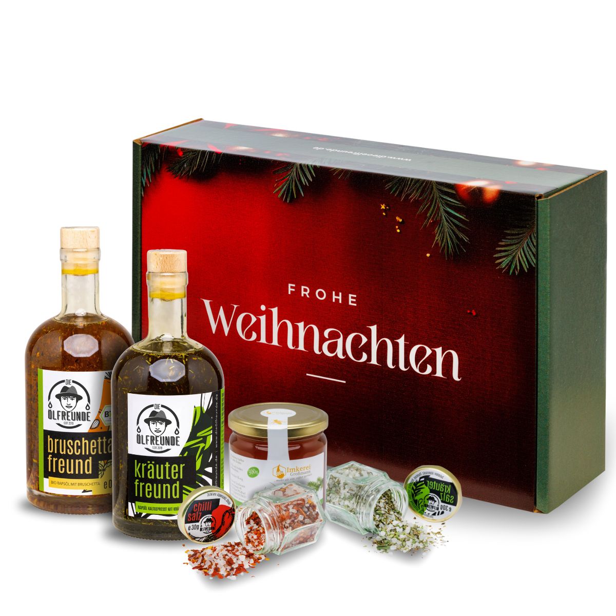 Eine Flasche Bruschetta-Öl, eine Flasche Kräuter-Öl, ein Glas Chillisalz, ein Glas Kräutersalz der Marke Die Ölfreunde und ein Glas Honig der Imkerei Großmann. Produkte stehen vor einer Weihnachts-Geschenkverpackung.
