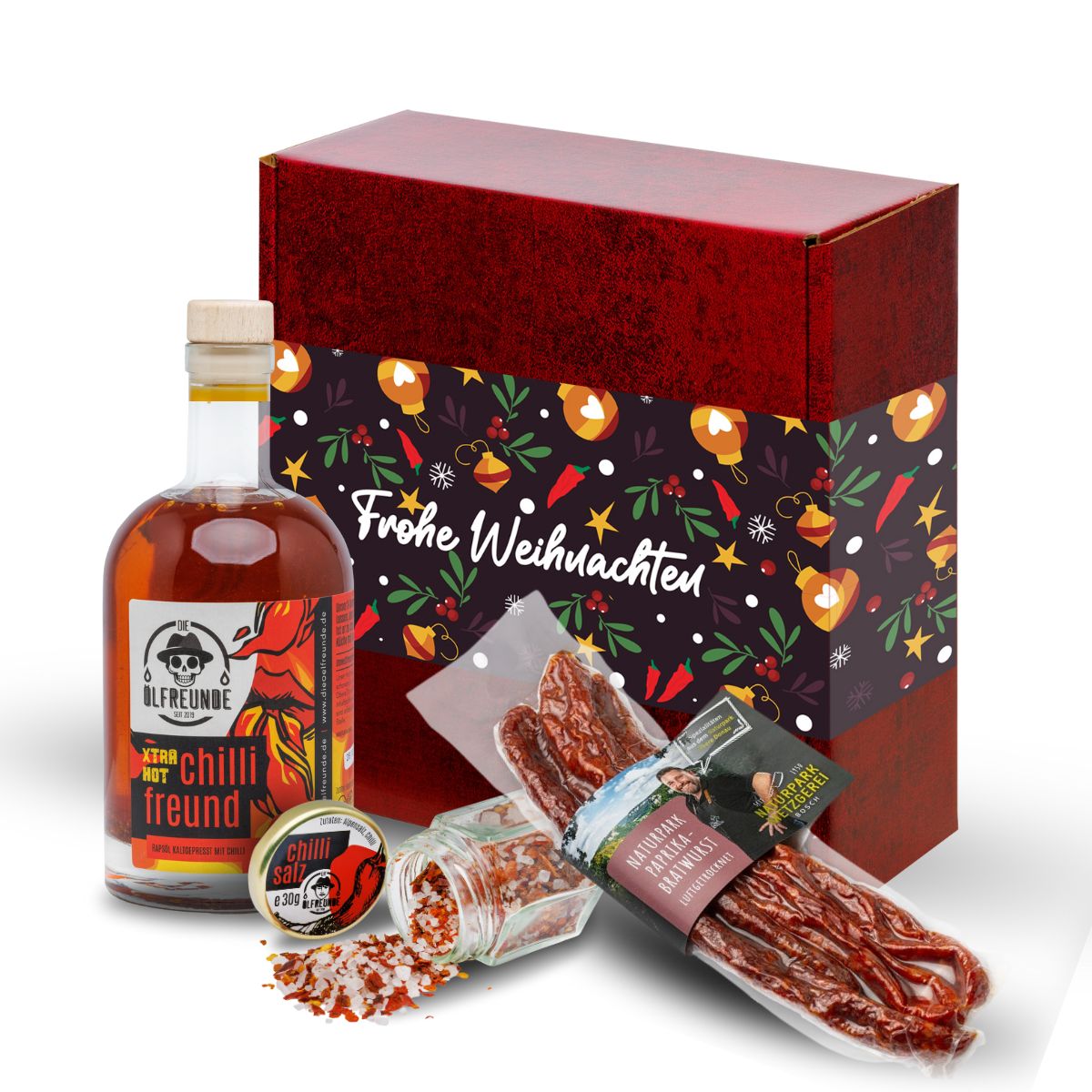 Eine Flasche Xtra Hot Chilliöl, ein Glas Chillisalz der Marke Die Ölfreunde und eine Packung Paprika Bratwurst der Marke Naturpark Metzgerei Bosch, vor einer Weihnaschts-Geschenkverpackung.