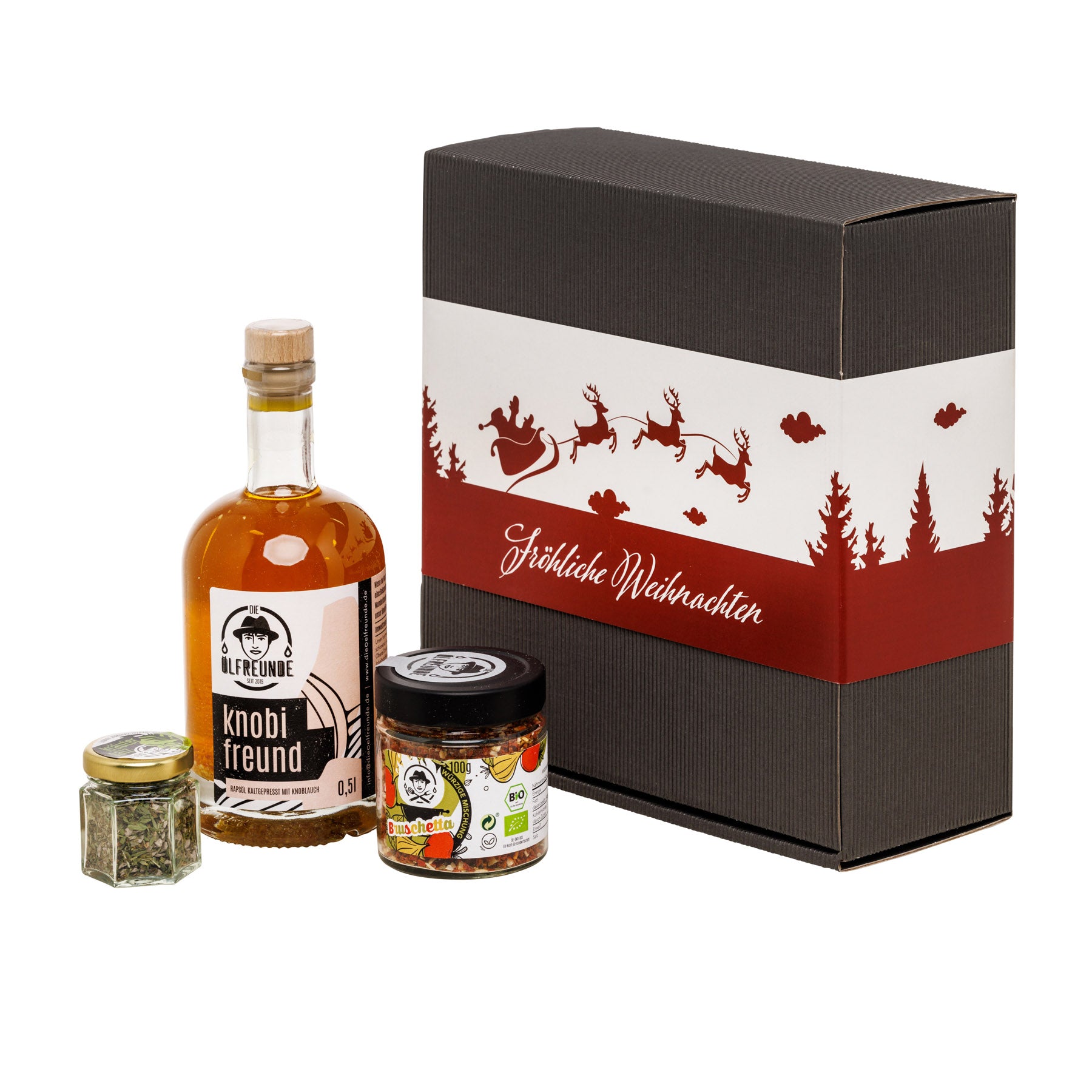 Eine Flasche Knoblauchöl, ein Glas Bruschetta-Gewürzmischung und ein Glas Kräutersalz der Marke Die Ölfreunde, vor einer Weihnachts-Geschenkverpackung