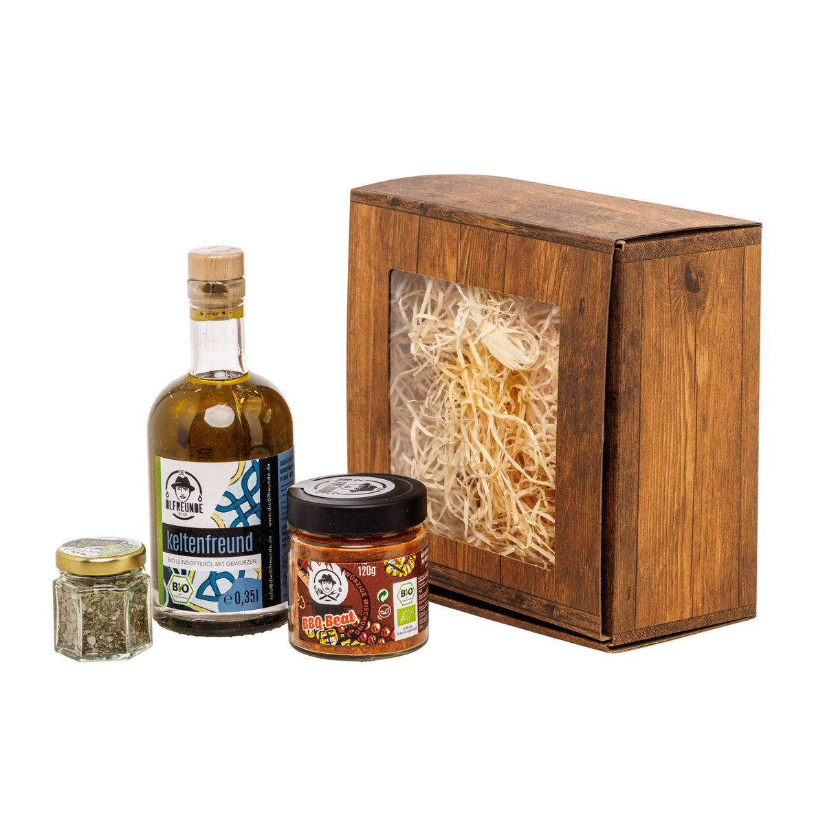 Eine Flasche Leindotteröl mit Gewürzen, ein Glas BBQ-Beat Gewürzmischung und ein Glas Kräutersalz der Marke Die Ölfreunde, vor einer Geschenkverpackung.