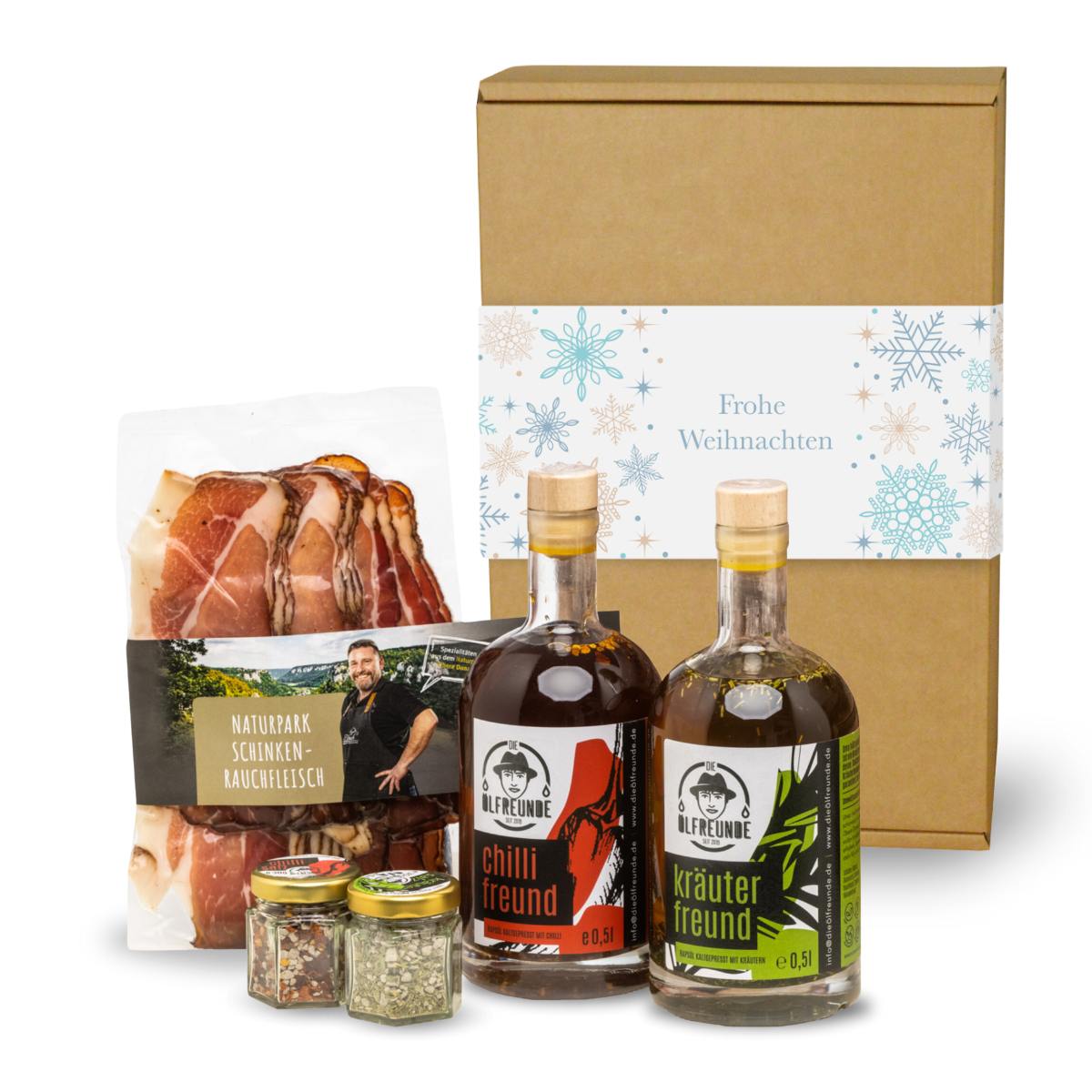 Kräuteröl, Chilli-Öl, Kräutersalz und Chillisalz der Marke Die Ölfreunde sowie Schinken-Rauchfleisch der Marke Naturpark vor einer Weihnachts-Geschenkverpackung.