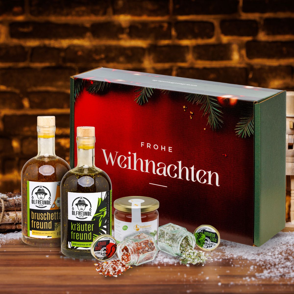 Bruschettaöl, Kräuteröl, Kräutersalz, Chillisalz der Marke Die Ölfreunde und Waldhonig der Imkerei Großmann, vor einer Weihnachts-Geschenkverpackung.
