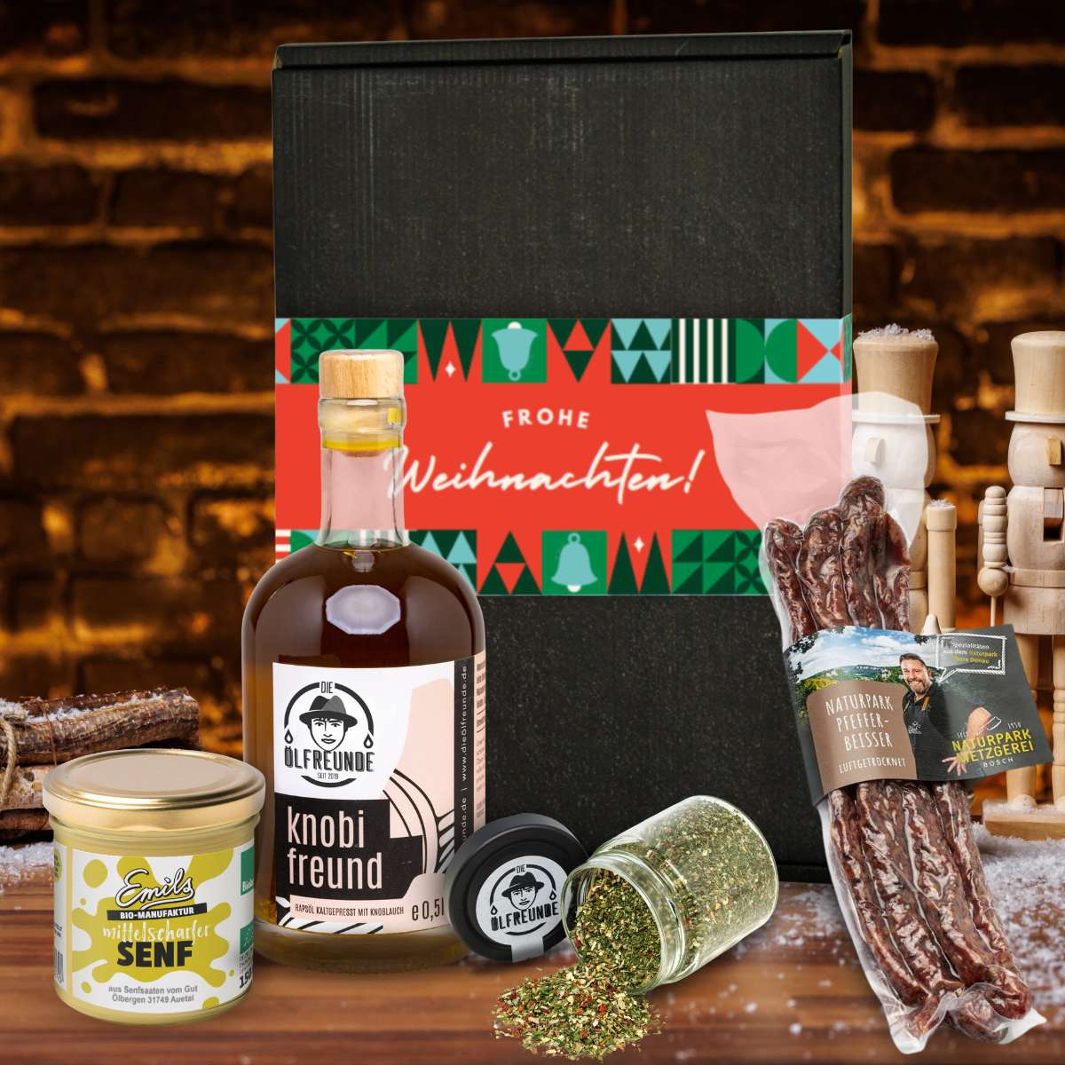 Knoblauchöl und Gewürzglas der Marke Die Ölfreunde, Pfeffer-Beisser der Marke Naturpark Metzgerei Bosch und mittelscharfer Senf der Marke Emils Bio-Manufaktur, vor einer Weihnachts-Geschenkverpackung und dunklem Hintergrund.