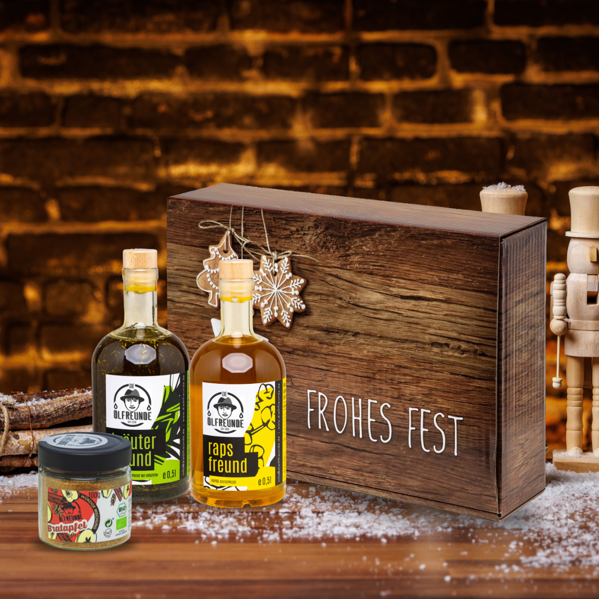 Kräuteröl, Rapsöl und Bratapfelgewürz der Marke Die Ölfreunde vor einer Weihnachts-Geschenkverpackung und einem dunklen Hintergrund.