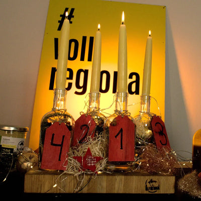 Vier Kerzen in Nummerierten Flaschen, daneben Produkte der Marke Die Ölfreunde. Im Hintergrund befindet sich ein gelbes Schuld mit einer Aufschrift.