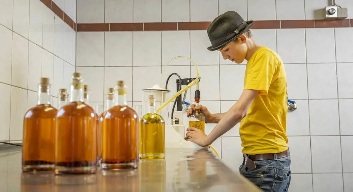 Eine Person mit schwarzen Hut und gelben T-Shirt, die dabei ist Öl in eine Flasche abzufüllen.