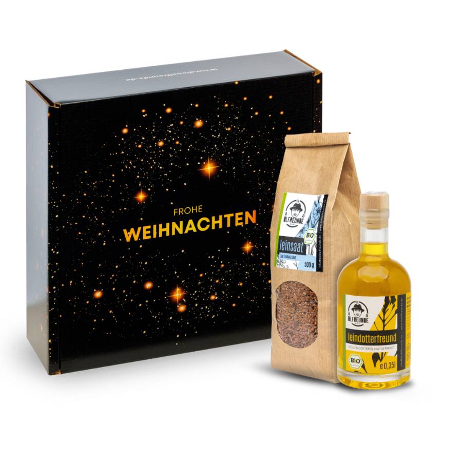 Eine Flasche Leindotter-Öl und ein Pack Leinsaat der Marke Die Ölfreunde vor einer Weihnachts-Geschenkverpackung.