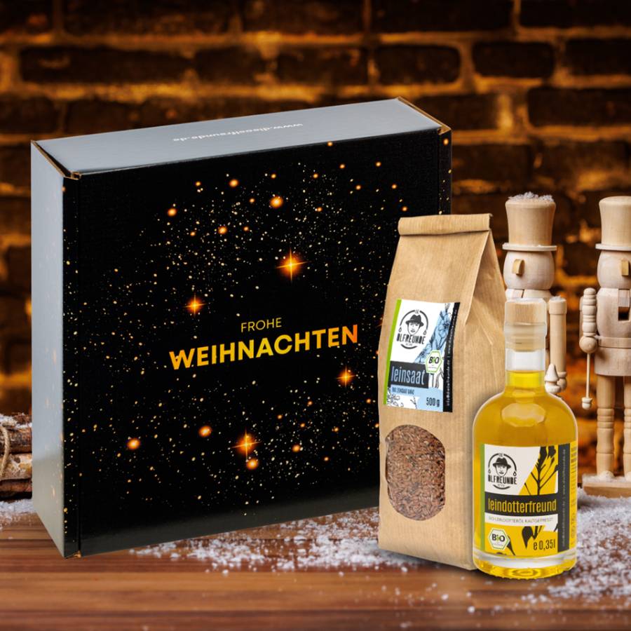 Eine Flasche Leindotter-Öl und ein Pack Leinsaat der Marke Die Ölfreunde vor einer Weihnachts-Geschenkverpackung und zwei holz-Nussknackern.