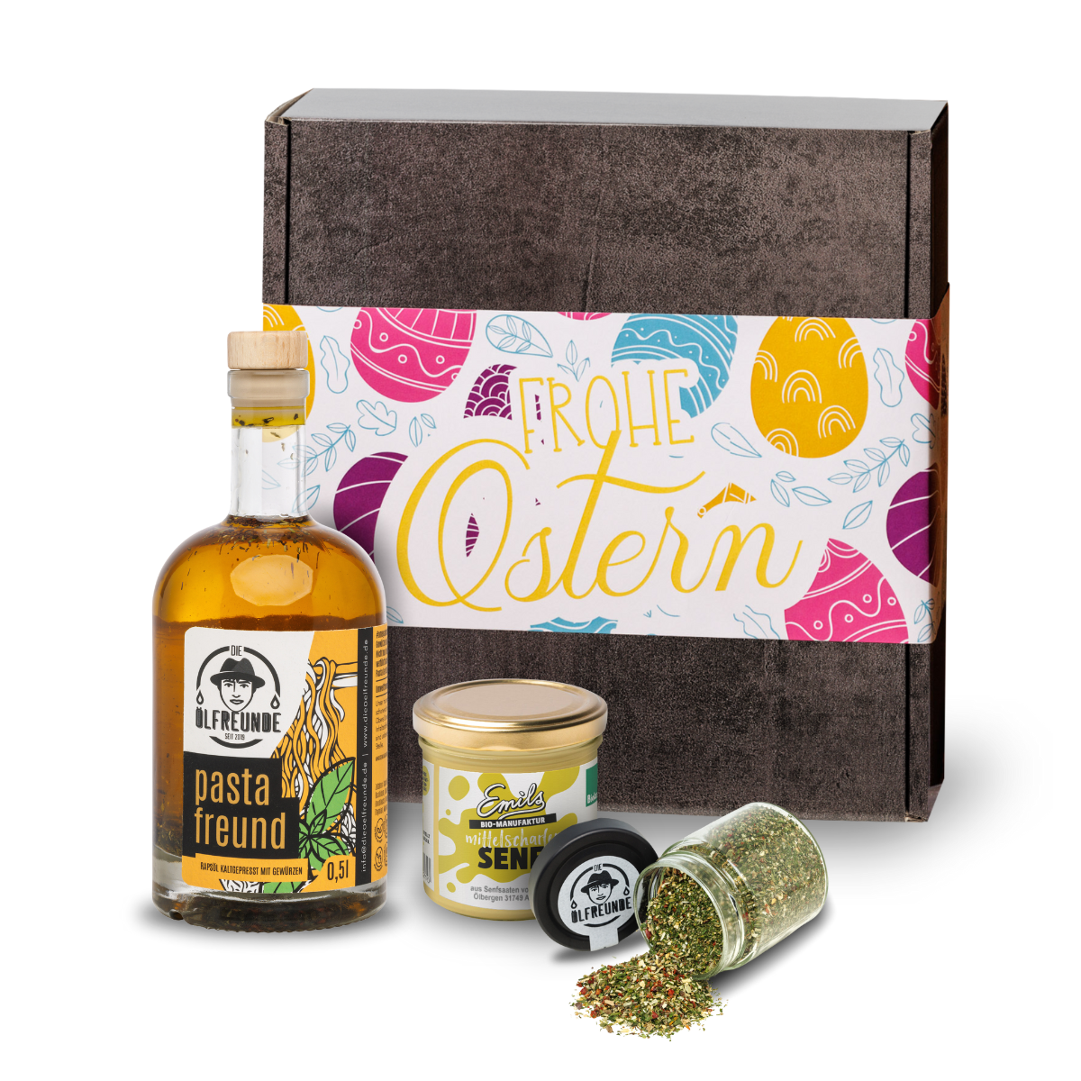Mittelscharfer Senf der Marke Emils Bio-Manufaktur, Pasta-Öl und ein Glas mit einer Gewürzmischung der Marke Die Ölfreunde, vor einer Oster-Geschenkverpackung.