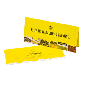 Zwei Gelbe, rechteckige Karten. Die eine liegt auf einem weißen Untergrund, mit der Aufschrift 'gutschein', die andere Karte steht aufrecht mit der Aufschrift 'fette überraschung für dich!'. Unter der Aufschrift sind Bilder von der Natur. Beide Karten sind mit dem Logo der Ölfreunde versehen.
