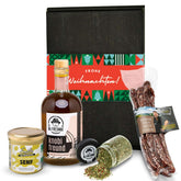 Weihnachtliches Feinkost-Set mit Bio-Senf, Knoblauchöl, Gewürzen und luftgetrockneten Pfefferbissen vor Geschenkbox mit Festband. Perfekt als stilvolles Präsent für Genießer.